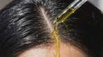macro close-up of a glass pipette dripping yellowish earthy green olive oil onto a wet black-haired scalp in direct sunlight

